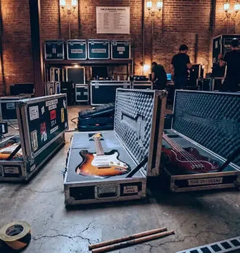 Guitars in open cases on a concrete floor with brick walls and people in the background.