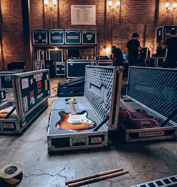 Guitars in open cases on a concrete floor with brick walls and people in the background.