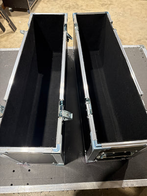 Two open silver metal flight cases with black foam interiors, placed side by side on a dark surface in a warehouse setting.